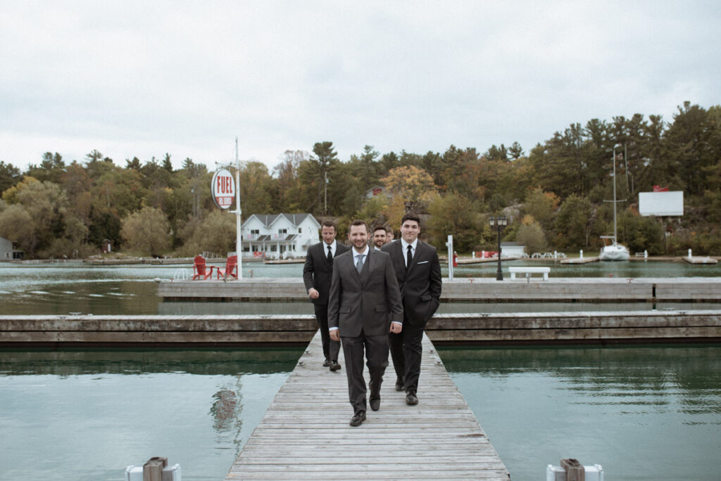 Killarney Mountain Lodge Wedding groom walking on a dock with his groomsmen following behind him. 