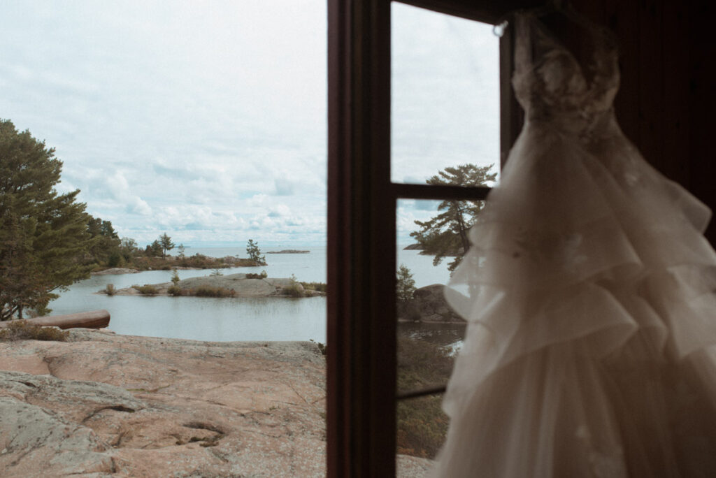 Killarney Mountain Lodge Wedding - window with Georgian Bay and pink rocks. A wedding dress is blurry on the right side. 