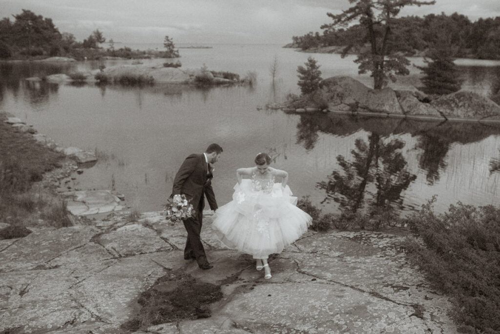 Killarney Mountain Lodge Wedding couple walking up a rock with Georgian Bay in the background. 