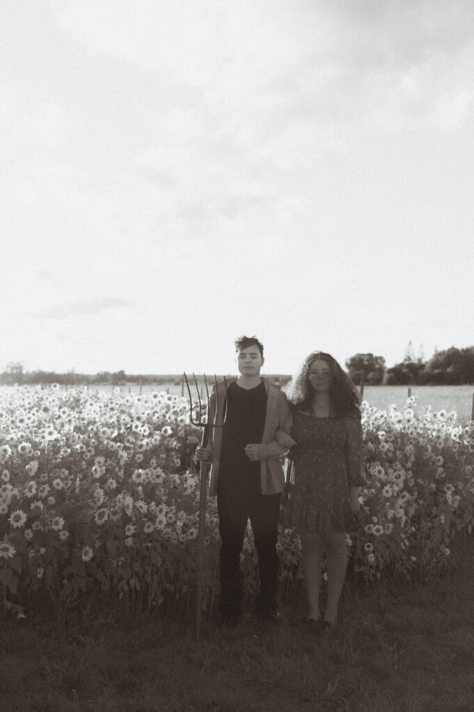 Couple in field with pitchfork in a sunflower field.