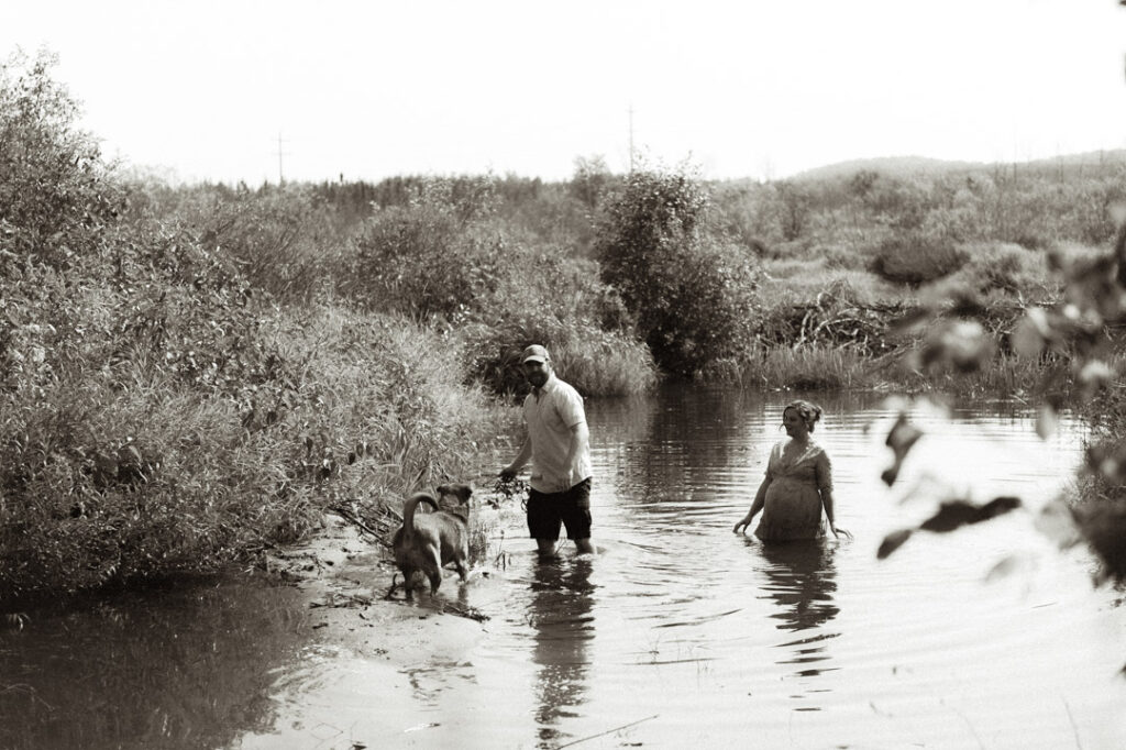 male and pregnant female couple in a river with a dog by an Ontario Documentary Photographer 