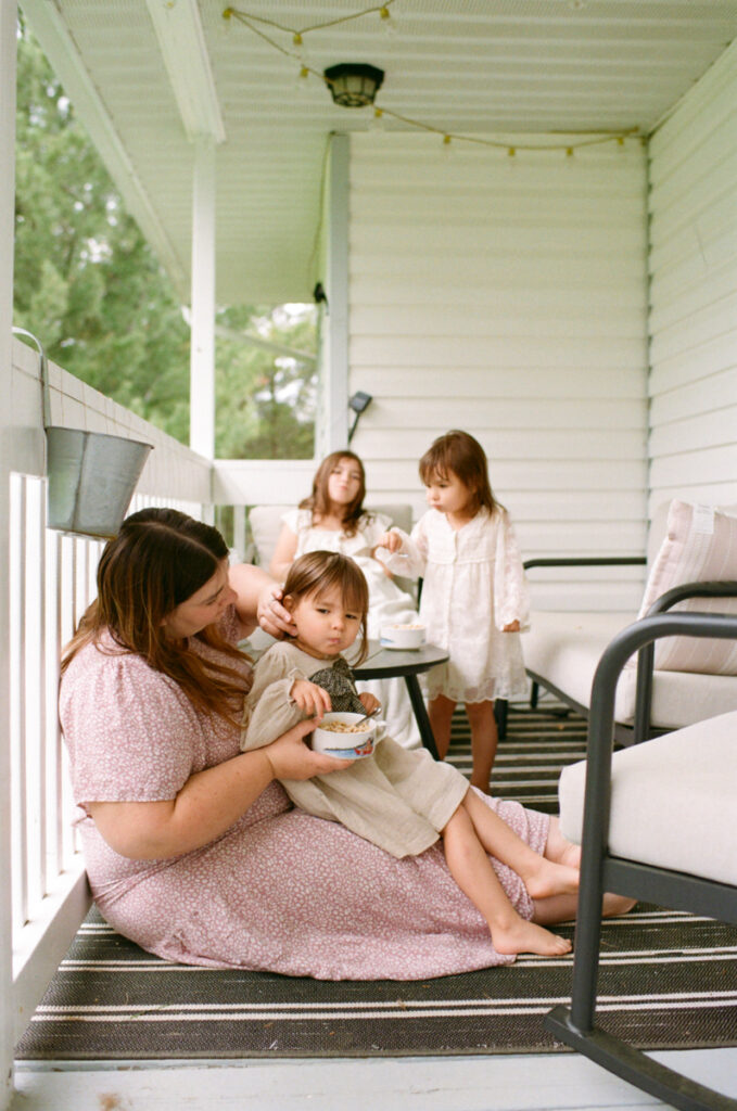 A mom and her 3 daughters on the front porch eating cereal documented by a Sudbury motherhood photographer
